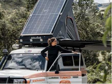 Viajera asomada a un Land Cruiser con carpa de techo y panel solar